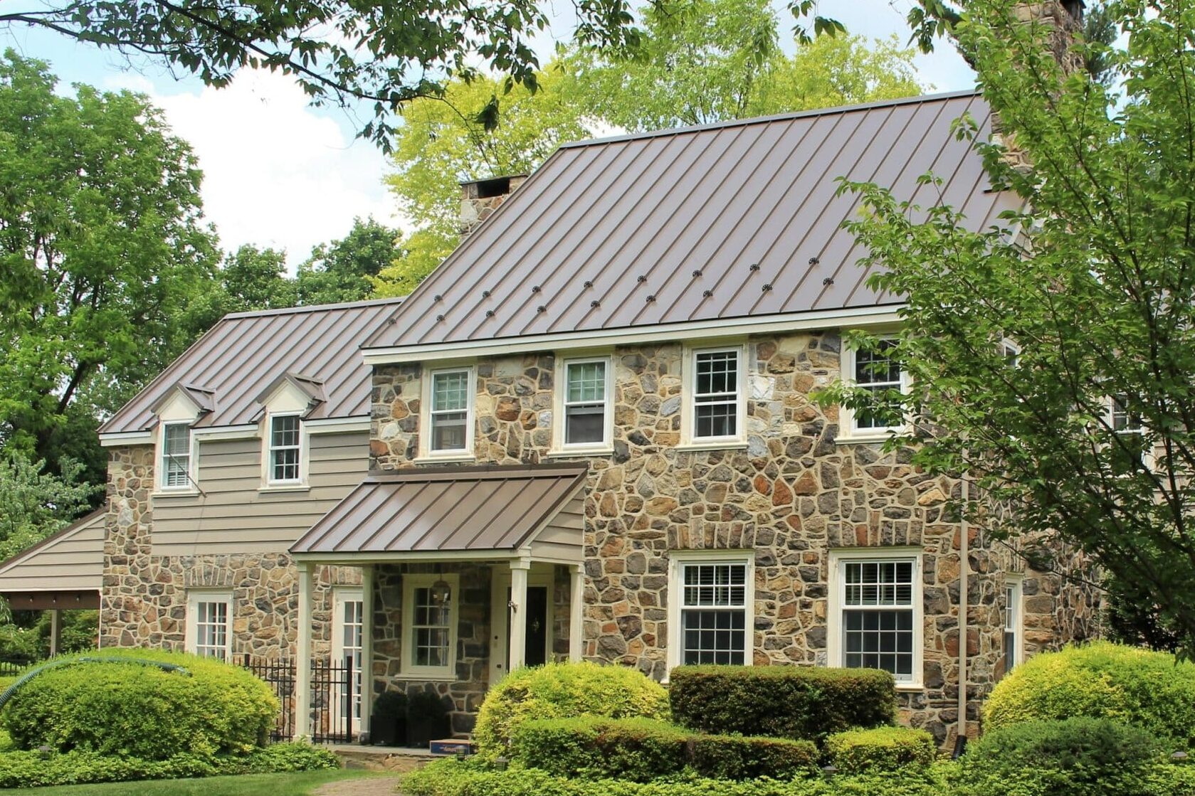 Grey standing seam metal roof on a large house with stone siding